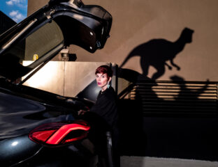 Jurassic Street, donna dietro a una macchina con cofano aperto di alto, sullo sfondo ombre di velociraptor - foto di Massimiliano Faralli